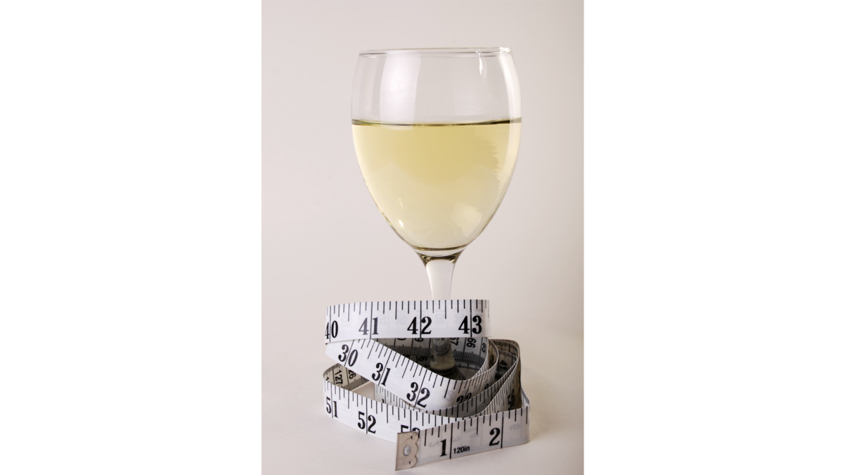 White wine in a glass with a tape measure around the stem