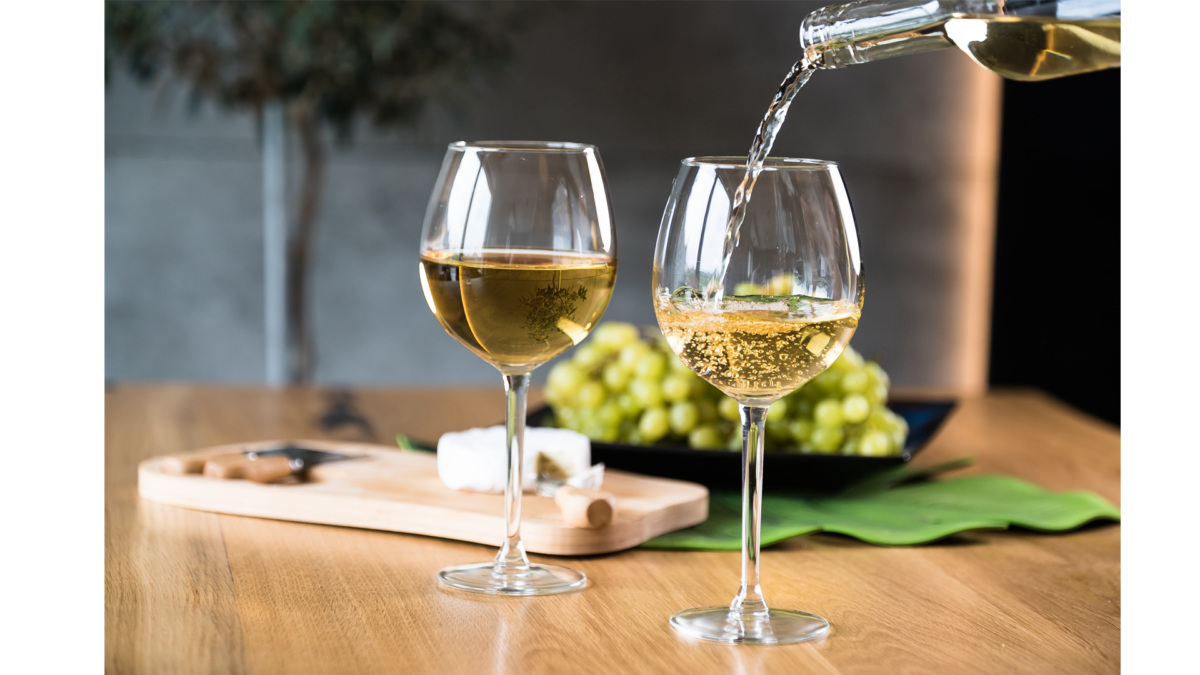 White wine is being poured into a glass. Cheese and grapes in background